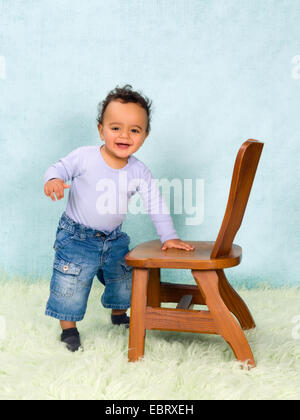 Adorable African baby boy trying to stand with help of a chair Stock Photo