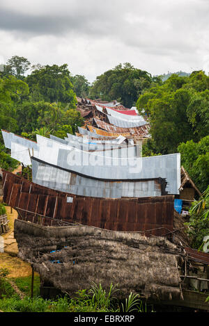 Row of scenic buildings in traditional village, with typical boat shaped roofs, set amid lush green rainforest. Mamasa region, W Stock Photo