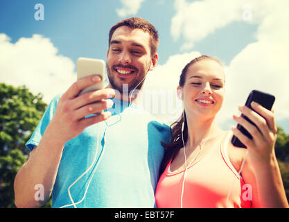 two smiling people with smartphones outdoors Stock Photo