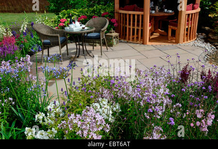 The patio area in a reflective aquatic garden with colourful flower border and seating Stock Photo