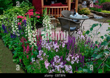 The patio area in a reflective aquatic garden with colourful flower border Stock Photo