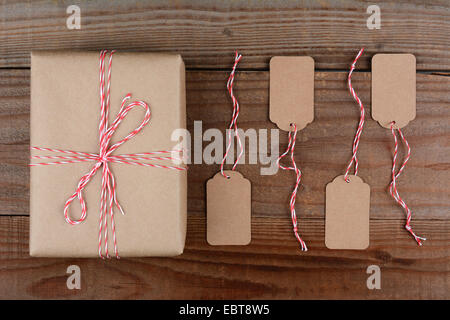 Overhead shot of a Christmas Package wrapped in plain brown paper and tie with red and white string. Four blank tags are next to Stock Photo