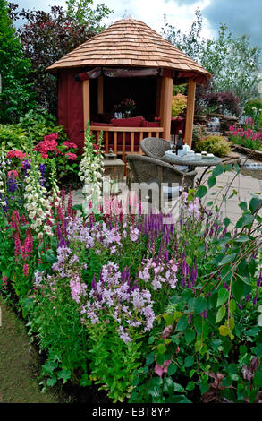 The patio area in a reflective aquatic garden with colourful flower border Stock Photo