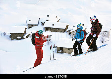 three young skiers on a snow-covered slope over the roofs of the winter sports resort, France, Savoie, Sainte Foy Stock Photo