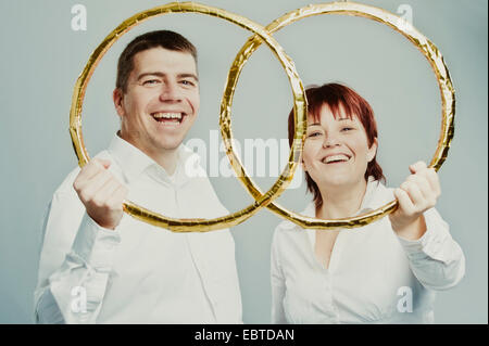 young couple happily looking through oversize wedding rings Stock Photo