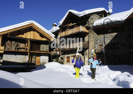 two women with skiing equipment walking through mountain village, France, Savoie, Sainte Foy Tarentaise Stock Photo