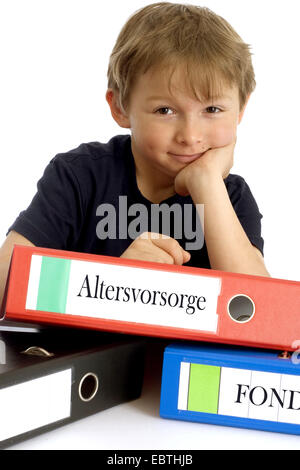 little boy smirking while leaning on a file with the inscription 'Altersvorsorge' ('retirement planning') Stock Photo