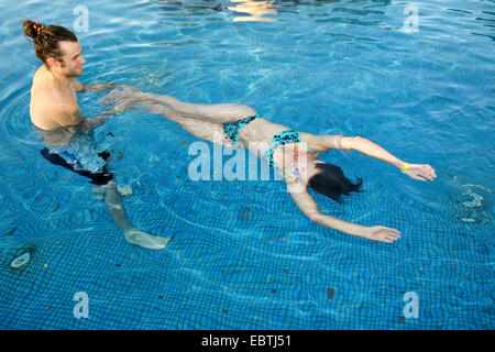 young man standing in a swimming pool pulling a young woman through the water Stock Photo