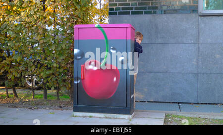 boy hiding behind a panelboard, painted with a cherry immersed in a drink, Germany, North Rhine-Westphalia, Duesseldorf Stock Photo