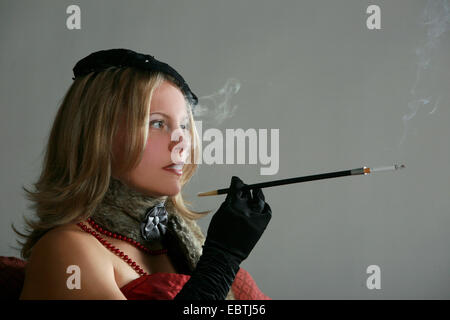 pretentiously dressed young woman smoking a cigarette sticked into a long mouthpiece Stock Photo