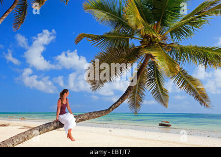 young woman sitting on palm tree at exotic sandy beach, Tanzania, Sansibar