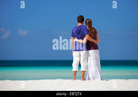 young couple embracing on tropical beach and looking to the sea Stock Photo