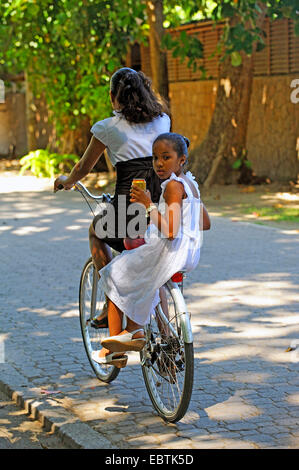 two young girls cycling together on a bike, Seychelles Stock Photo