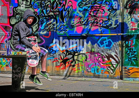 11 years old boy sitting in front of a graffiti wall with a skateboard, Germany, North Rhine-Westphalia, Cologne Stock Photo