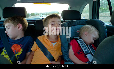 three little boys sleeping side by side on the backseat of a car Stock Photo
