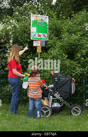 mother explaining an information sign at playground to her son , Germany, North Rhine-Westphalia Stock Photo