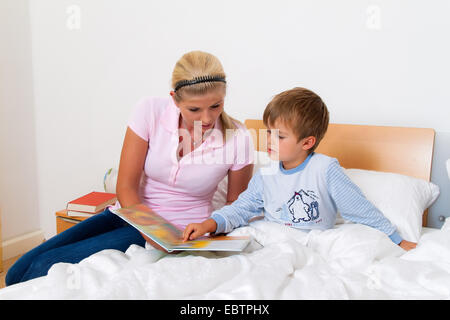mother sitting at the bedside and reading a book with her sick child
