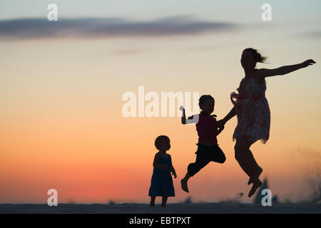 silhouettes of mother and two children jumping on beach at sunset