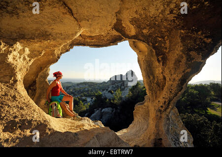 female wanderer sitting in rock window and enjoying the view, France, Provence, Les Alpilles, Baux de Provence Stock Photo