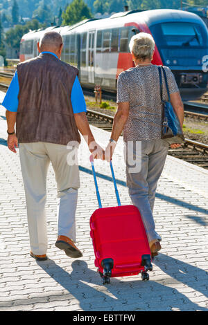 elderly couple carrying a suitcase together on a railway plattform Stock Photo