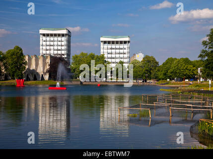 two young people sitting on a bench at the city lake with the two town hall towers in the background reflecting in the water, Germany, North Rhine-Westphalia, Ruhr Area, Marl Stock Photo