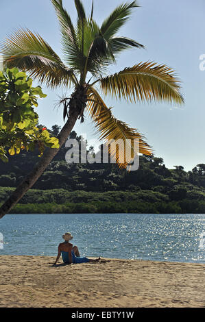woman sitting under palm tree at sandy beach, Madagascar, Nosy be Stock Photo