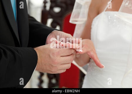 bridegroom putting wedding ring on brides finger Stock Photo