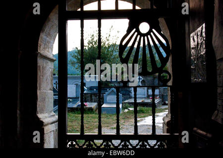 view through a iron gate with a pilgrims shell of the cemetery of Iglesia de Santiago, Spain, Galicia, Lugo, Triacastela Stock Photo