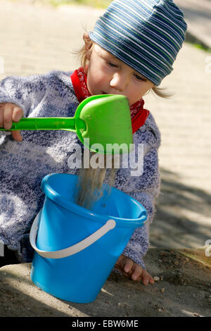 little boy shoveling sand in a pail, Germany Stock Photo