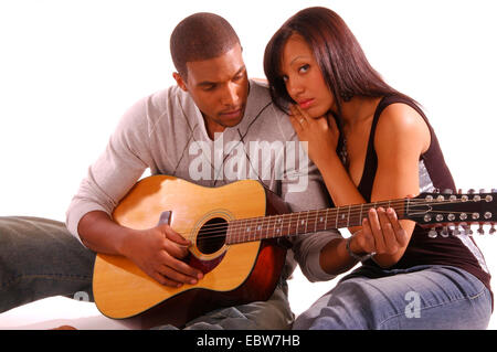 young, dark skinned couple nestling to each other while the man plays on the guitar Stock Photo