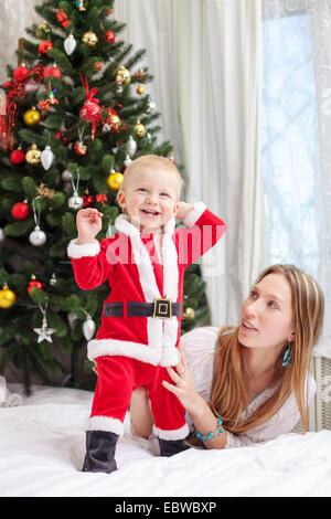 Young mother playing with baby dressed in Santa costume Stock Photo