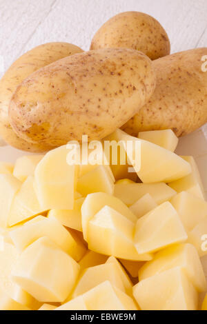 Three Whole Potatoes and Chopped Peeled Pieces on Cutting Board Stock Photo