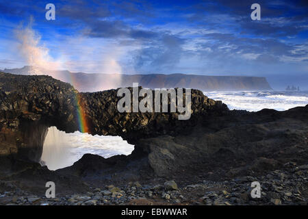 Dyrholaey cliff in the foreground a wave breaking on the reef, creating a rainbow, Iceland. Stock Photo