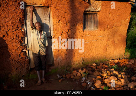 young man standing in front of mud house in early morning, Burundi, Cancuzo, Cankuzo