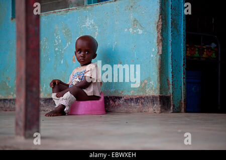 little boy sitting on a potty in front of a house, Burundi, Bujumbura Marie, Bujumbura Stock Photo