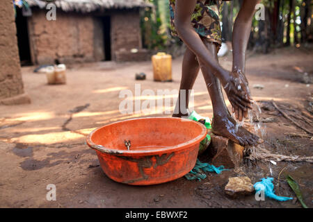 young woman in traditional African clothes washing herself in front of her mud house in the morning, Burundi, Karuzi, Buhiga Stock Photo