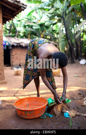 young woman in traditional African clothes washing herself in front of her mud house in the morning, Burundi, Karuzi, Buhiga Stock Photo