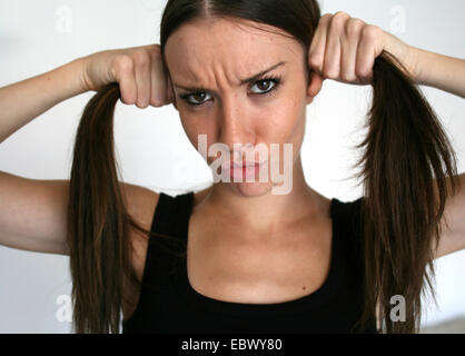 young woman pouting while forming two braits of her brunette long to hair Stock Photo