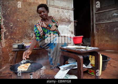 woman is baking a bread called Chapati made of mais flour on a charcole oven in front of a simple house, Uganda, Jinja Stock Photo