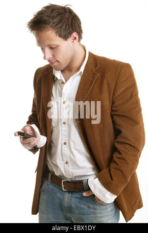 young man in a white shirt and brown jacket, writing an SMS with a hand in the pocket Stock Photo