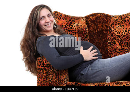 pregnant mother sitting in a leopard armchair holding her belly Stock Photo
