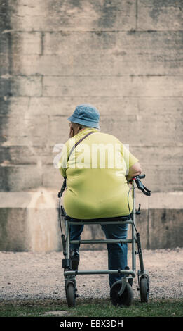 Senior woman sitting on walker in front of stone wall Stock Photo