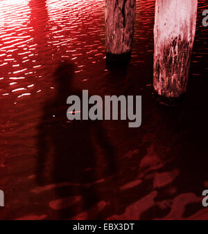 Ominous shadow of person in red water under a pier Stock Photo