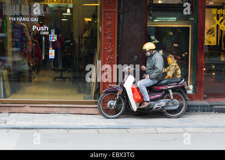 Vietnamese man on a moped texting on his mobile phone. Outside a shop in Hanoi. Stock Photo