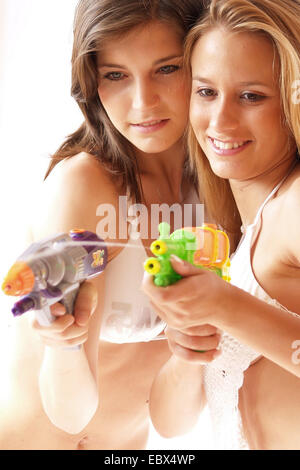two long-haired young women in bikinis standing close together shooting with water pistols with a smile Stock Photo