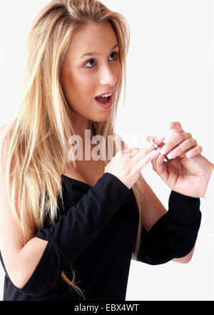 long-haired blond young woman in a evening dress looking up dreamily putting a ring on her finger Stock Photo