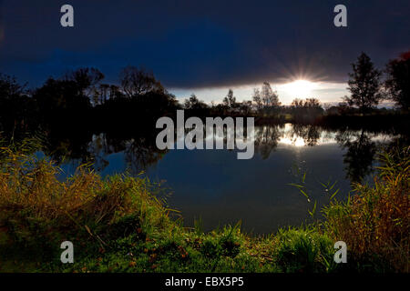 setting sun shining on a lake through a hole in a cloud cover, Germany, Lower Saxony, Vogtlaendische Schweiz, Dorum-Neufeld Stock Photo
