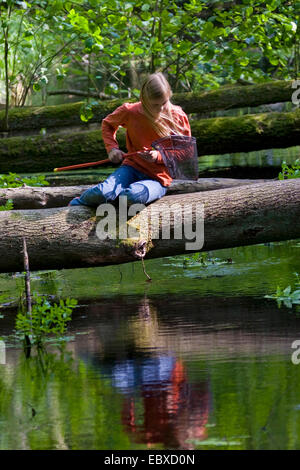 girl with dip net at a forest creek, sitting on a tree trunk over the water Stock Photo