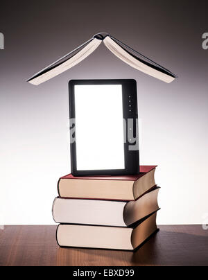 Open book hovering over a stack of printed books and e-book. Stock Photo