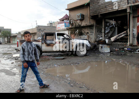 Kirkuk, Iraq. 5th Dec, 2014. A boy stands in front of a damaged car at an explosion site in the city of Kirkuk, Iraq, Dec 5, 2014. A suicide bomber with an explosive vest blew himself up in a cafe in the northern Iraqi city of Kirkuk, killing at least 15 people and wounding 20 others on Dec. 4, a local police told Xinhua on condition of anonymity. © Dena Assad/Xinhua/Alamy Live News Stock Photo